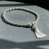 A large Tassel charm silver bracelet sat on a grey stone tray