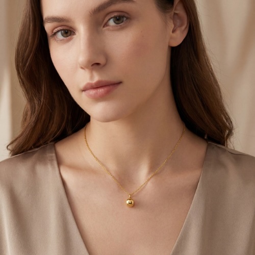 Model with dark brown hair and brown eyes wearing a gold Ball necklace